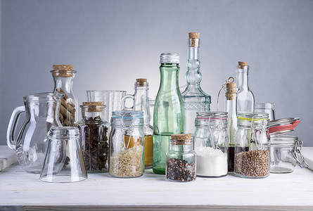 静物画的透明玻璃瓶、 罐和白色的木桌上的眼镜.