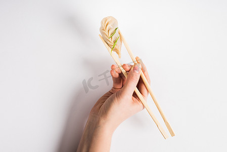 delicious摄影照片_cropped view of woman holding delicious Chinese boiled dumpling with chopsticks on white background