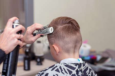 后视镜漂亮的欧洲男孩在理发店里做发型。理发师为男孩做发型