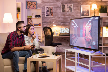 玩电子游戏摄影照片_男人坐在沙发上，在电视上玩电子游戏