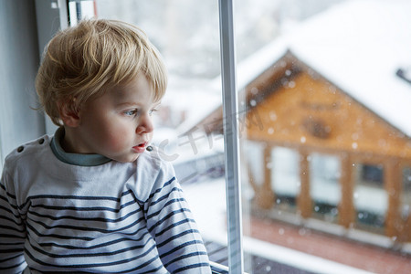 蹒跚学步的小男孩在冬天里望着窗外