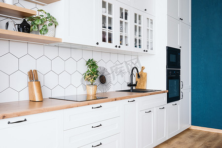 Side view of modern kitchen interior design with blue wall. White wood furniture, appliances and decor. Spacious apartment after renovation. Bright real estate for sale