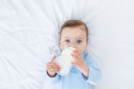 男婴穿着蓝色的紧身衣睡觉前吃床上瓶子里的牛奶，婴儿食品的概念