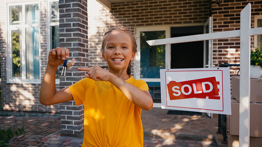 一个快乐的孩子指着靠近木板的钥匙，手里拿着卖出的信笺和新房子