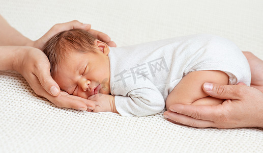 父母摄影照片_出生在家庭手中。婴儿睡在白色毛毯上的妈妈和爸爸的手掌里。抱着梦想的父母可爱的小孩脸肖像。生育和养育子女