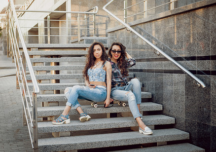 两个年轻的混血女孩在休闲服装步行与滑板周围的街道