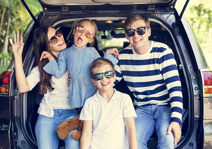 去旅行摄影照片_父母和孩子们在太阳镜下坐在汽车车厢里, 家人正在去旅行。