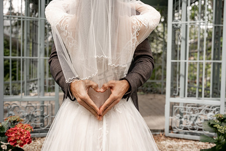 partial view of groom showing heart symbol with hands while embracing bride