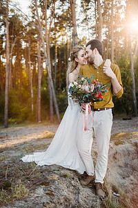 美丽的新娘的肩膀拥抱她的新郎。在森林里的婚礼走。新婚夫妇看着彼此。白色的裙子和橄榄色的衬衫的男人的女孩。图稿.