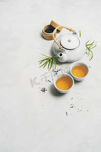 地图文字标签摄影照片_亚洲茶的概念，两杯白茶，茶壶，茶具，筷子，竹垫，周围都是白底干绿茶，上面有文字空间。 煮茶和喝茶.