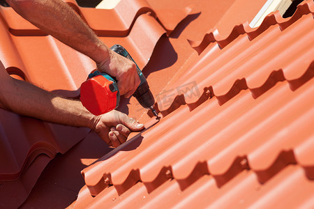 工人用电钻安装红色金属屋顶上平铺上木房子里