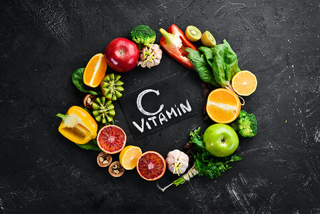 维生素c摄影照片_含有维生素C的水果和蔬菜：橙子、柠檬、苹果、玫瑰、大蒜、花椰菜、苹果、奇异果、菠菜。顶部视图。在黑色的石头背景上.