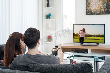亚洲对年轻夫妇华清高尔夫运动在电视上在家里