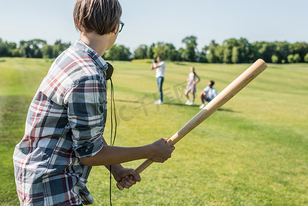 少年男孩拿着棒球棍在公园里和朋友玩的侧面视图