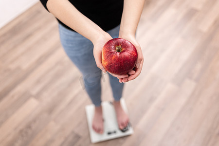 女人用秤量体重，手里拿着苹果.
