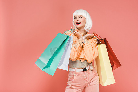 时髦的女人在白色假发与购物袋，隔离在粉红色