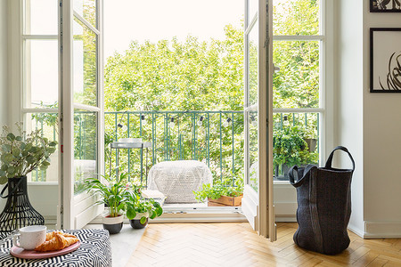 起居室摄影照片_在阳光明媚的阳台上打开玻璃门, 从起居室内部进入城市花园, 并配有舒适的家具