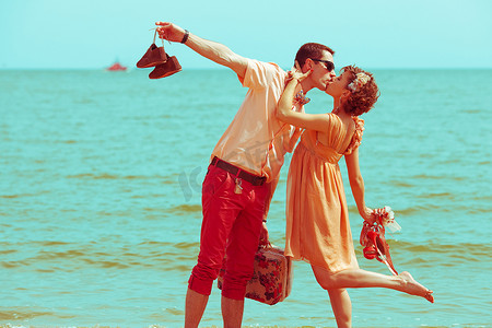 沙滩衣服摄影照片_沙滩上散步的情侣。快乐的年轻人结婚时尚及膝