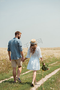 妇女在白色礼服的后面看法与狂放的花花束一起散步与男朋友在领域