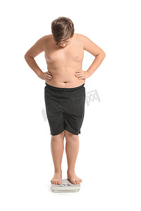 体重超标的男孩站在白色背景的天平上