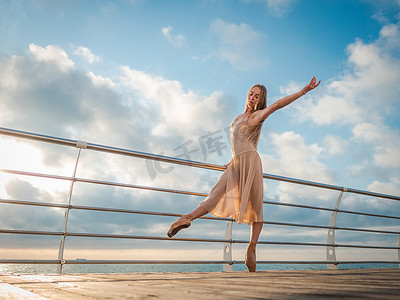 日出时在路基之上大洋或大海沙滩上跳舞芭蕾舞女演员在米色的丝绸衣服和普安特。年轻美丽的金发女子，长发练习与情感经典演习.