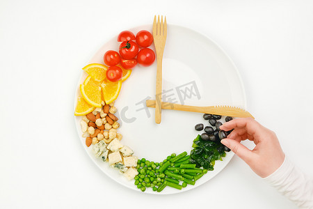 减肥瘦身操摄影照片_色彩斑斓的食物和餐具,以盘子上的钟的形式排列.橄榄在手。间歇性禁食、节食、减肥、午餐时间概念.