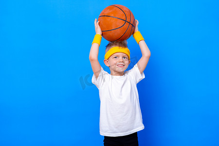 矮小摄影照片_一个身材矮小的小男孩,背负着蓝色工作室背景的篮球运动.体操运动。儿童运动员。活动。体育。健康、健康和精力。成功