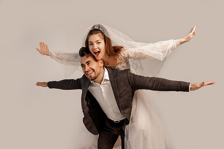 cheerful bride piggybacking on happy groom isolated on grey