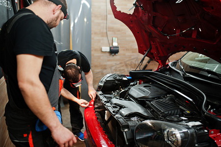 汽车维修人员在车辆维修车间的红色车体上贴上防石膜。带有特殊薄膜的汽车保护.
