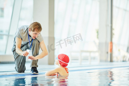 what摄影照片_Young trainer explaining little swimmer what to do in extreme situation in water