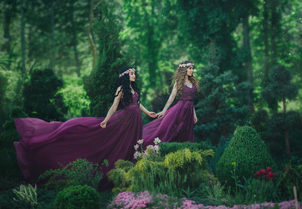 两个女朋友, 一个金发女郎和一个黑发女郎, 手牵着手。背景开花花园。公主们穿着豪华的紫色连衣裙, 长着一列火车, 风吹着一阵风。.