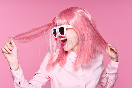 假发摄影照片_戴着粉色假发和太阳镜的漂亮女人，望着粉红的背景 