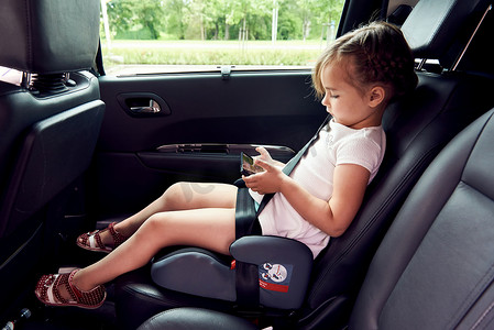 一辆车摄影照片_小女孩坐在一辆车，一款智能手机在手中
