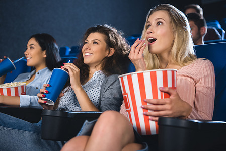 情绪化的多种族妇女与爆米花一起看电影在电影院