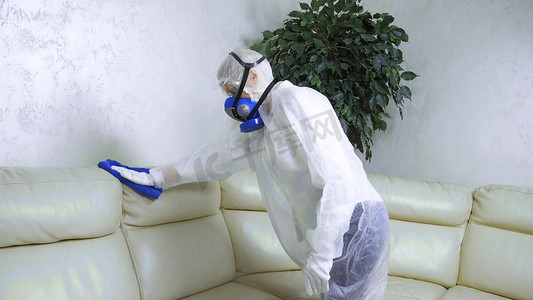穿着防护服和呼吸器的女人在房间里擦拭皮沙发.