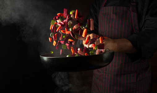 Cooking vegetables in a frying pan in the hands of a chef for a vegetarian food. Advertising space on a black background