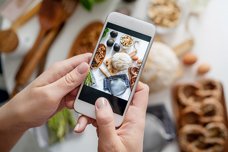 拿白摄影照片_食物博客写手带着她的手机在白桌子上拍照. 