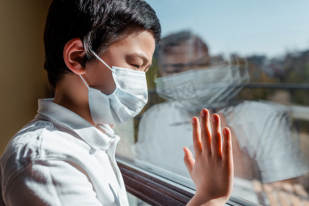 身穿医疗面罩的亚裔儿童在隔离窗口朝外看