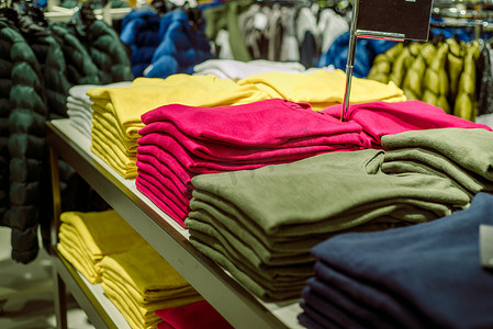 绿色女装摄影照片_商店里有汗衫，一堆堆叠好的针织品。黄色的绿色和紫色夹克。女装堆在商店的脚后跟上.