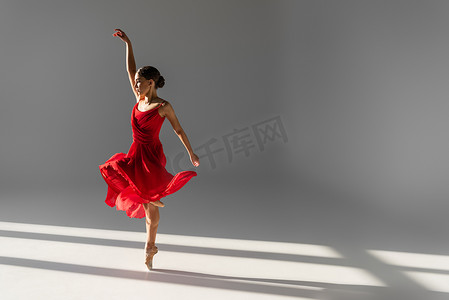穿着红色衣服、背景灰暗、阳光普照的年轻芭蕾舞演员的侧影