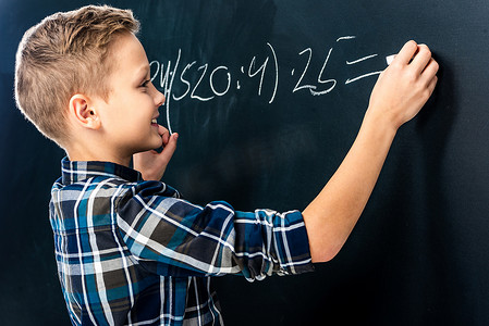 微笑的男孩用粉笔在黑板上写数学榜样