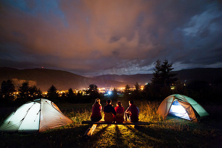 在晚上坐在营地和帐篷旁边的朋友