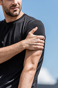 穿着黑色T恤的运动员在蓝天下肩部疼痛的裁剪视图