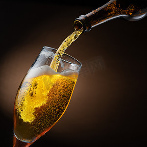 啤酒从瓶子里喷出，倒入啤酒杯，造成大量气泡和泡沫。深褐色背景.