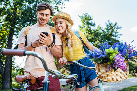 微笑的情侣使用智能手机在公园的夏天天
