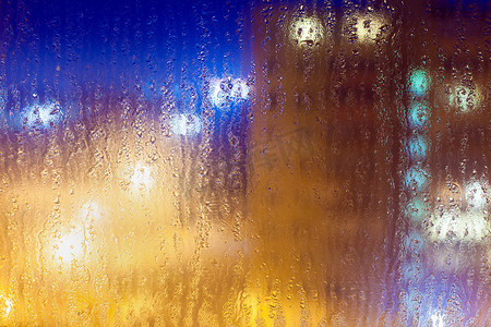 在雨天的潮湿玻璃上, 抽象的背景与浅色多彩的多色亮点.