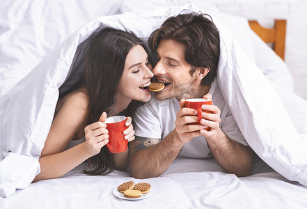 可爱的千禧年夫妇在爱在床上分享早餐