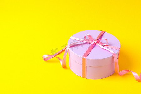 Round gift box with bow on yellow background