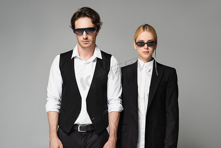 年轻夫妇戴着墨镜，身穿黑白相间的灰色衣服，站在镜头前
