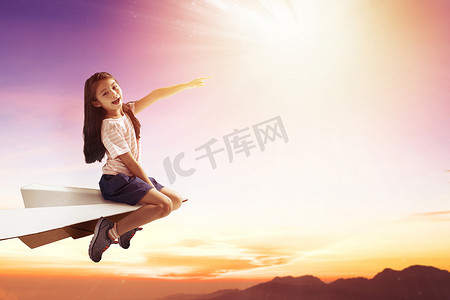 纸飞摄影照片_快乐的小女孩在纸飞机上，在天空中飞翔